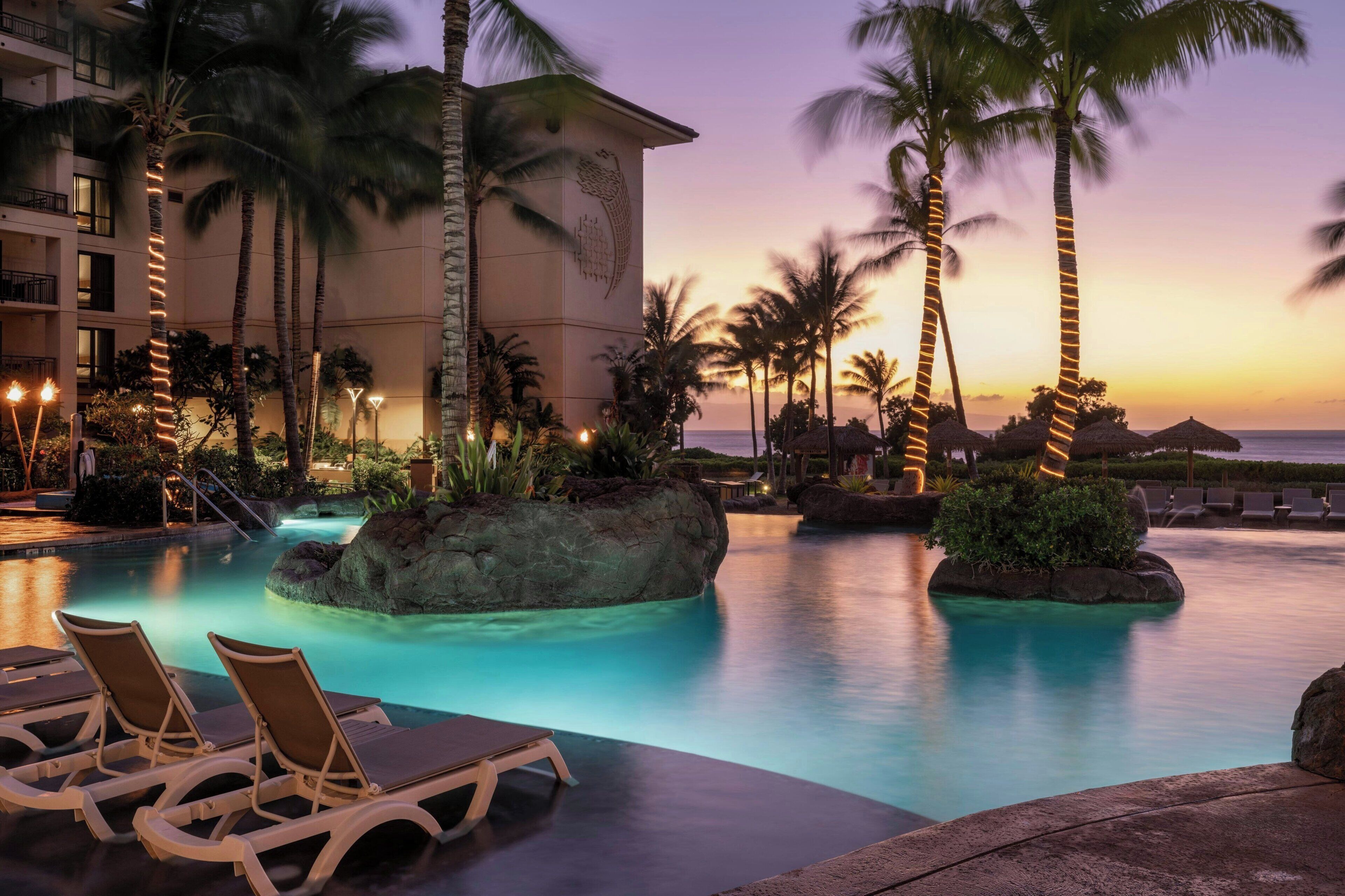 Una piscina en un resort con sillas de descanso, palmeras y un edificio de diseño singular.