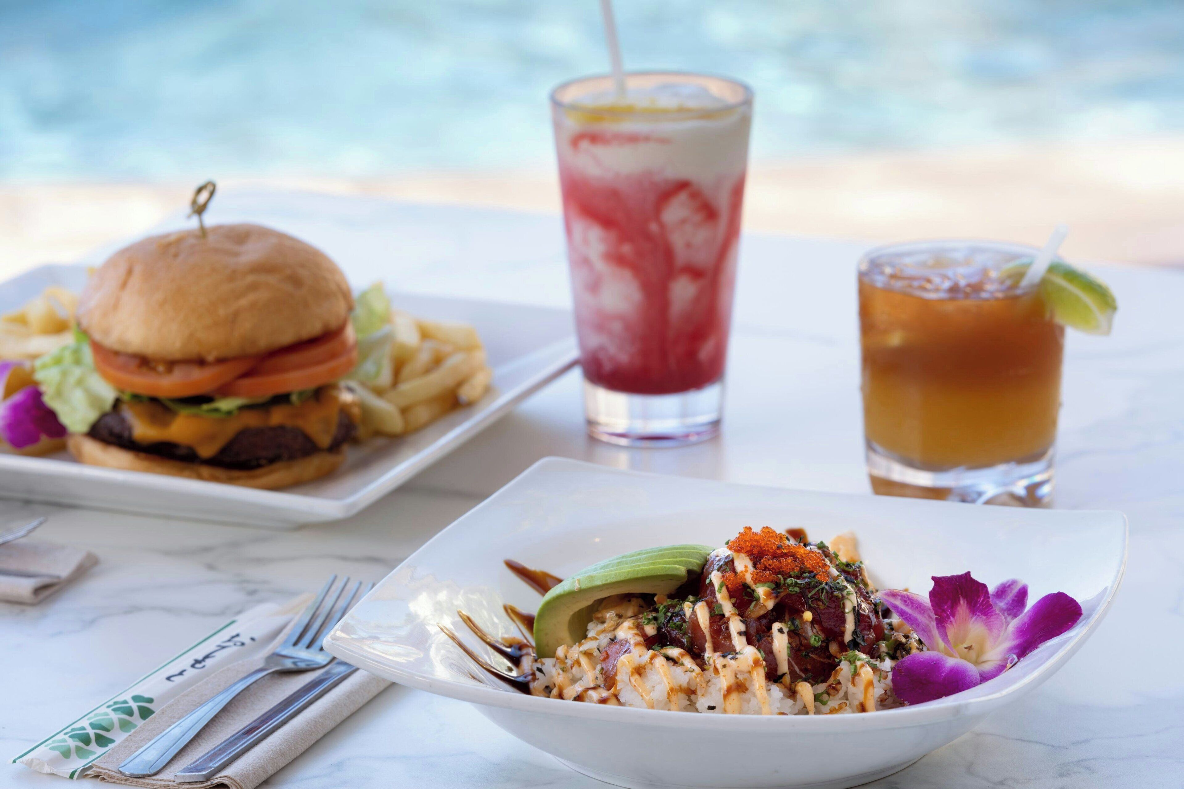 A dining table with a burger, fries, a drink, and a bowl of food.