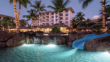 Un hotel con piscina, palmeras y una cascada.