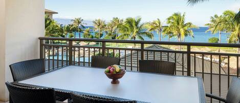 A balcony with a table and chairs, overlooking a beach with palm trees and the ocean.