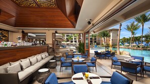 A modern outdoor lounge area with wicker furniture, a pool view, and a bar area.