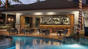 A poolside bar area with seating and a stone wall backdrop.