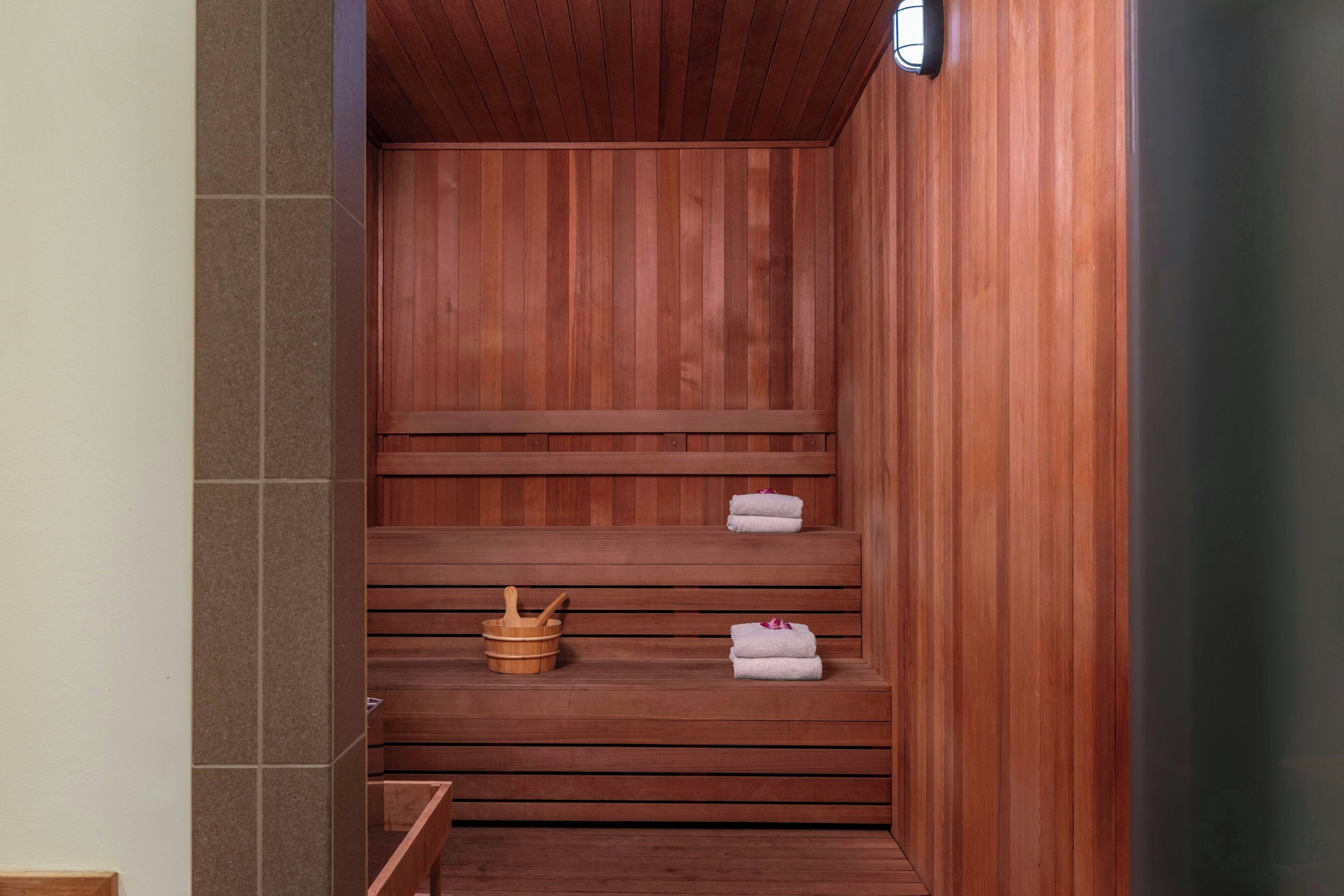 Una sauna de madera con varios bancos, un cubo de madera y toallas.