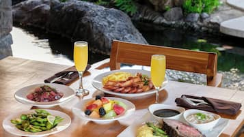 A table with various dishes including steak, fruits, and vegetables, set against a backdrop of a rocky garden and a pond.