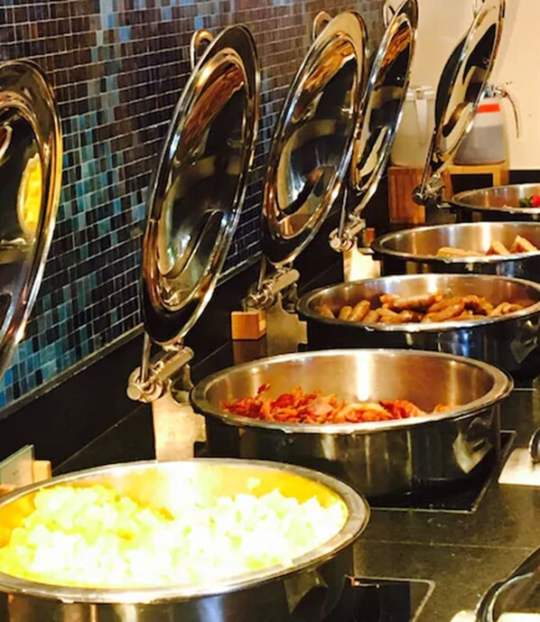 A buffet with various food items in metal serving dishes, some with lids.