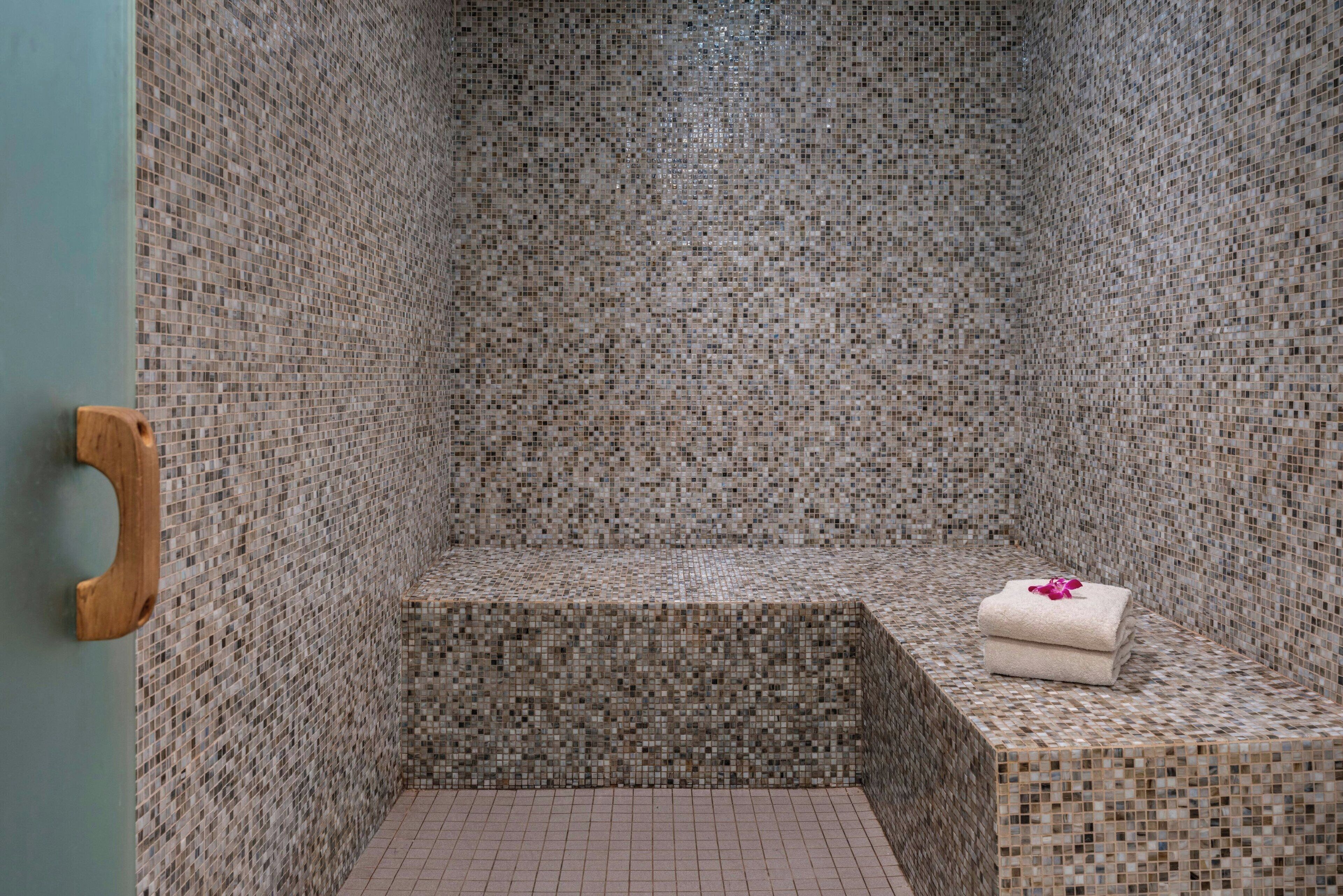 A bathroom with mosaic tile walls and a wooden door handle.