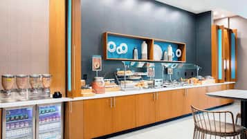 Una barra de desayuno moderna con diversas opciones de alimentos, bebidas refrigeradas y una estación de café.