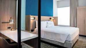 A hotel room with a bed, bedside table, lamp, and a large mirror.