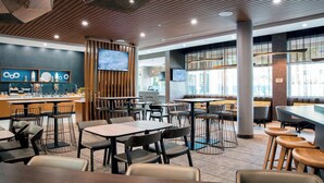 A modern restaurant with wooden ceiling panels, multiple tables and chairs, and large windows.