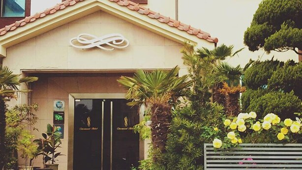 A building with a tiled roof, a large infinity symbol above the entrance, and a variety of plants and flowers around the entrance. - Charmant Hotel (Mokpo)