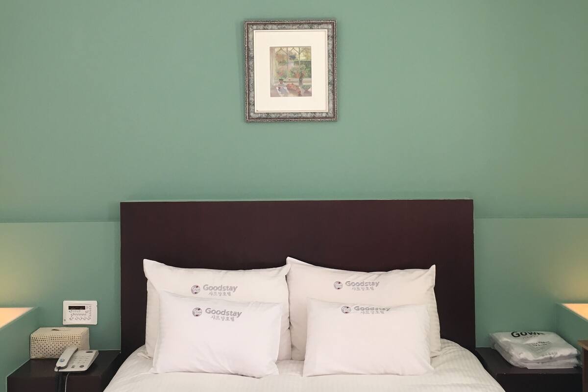 Une chambre d’hôtel avec un lit, deux oreillers, un tableau encadré, une table de chevet et une petite table.