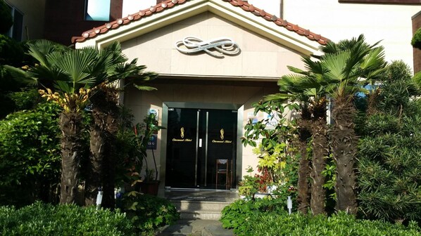 The entrance of a hotel with a tiled roof and a logo above the doors. - Charmant Hotel (Mokpo)