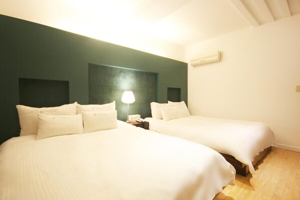 Una habitación con dos camas, una mesita de noche con lámpara y aire acondicionado instalado en la pared.