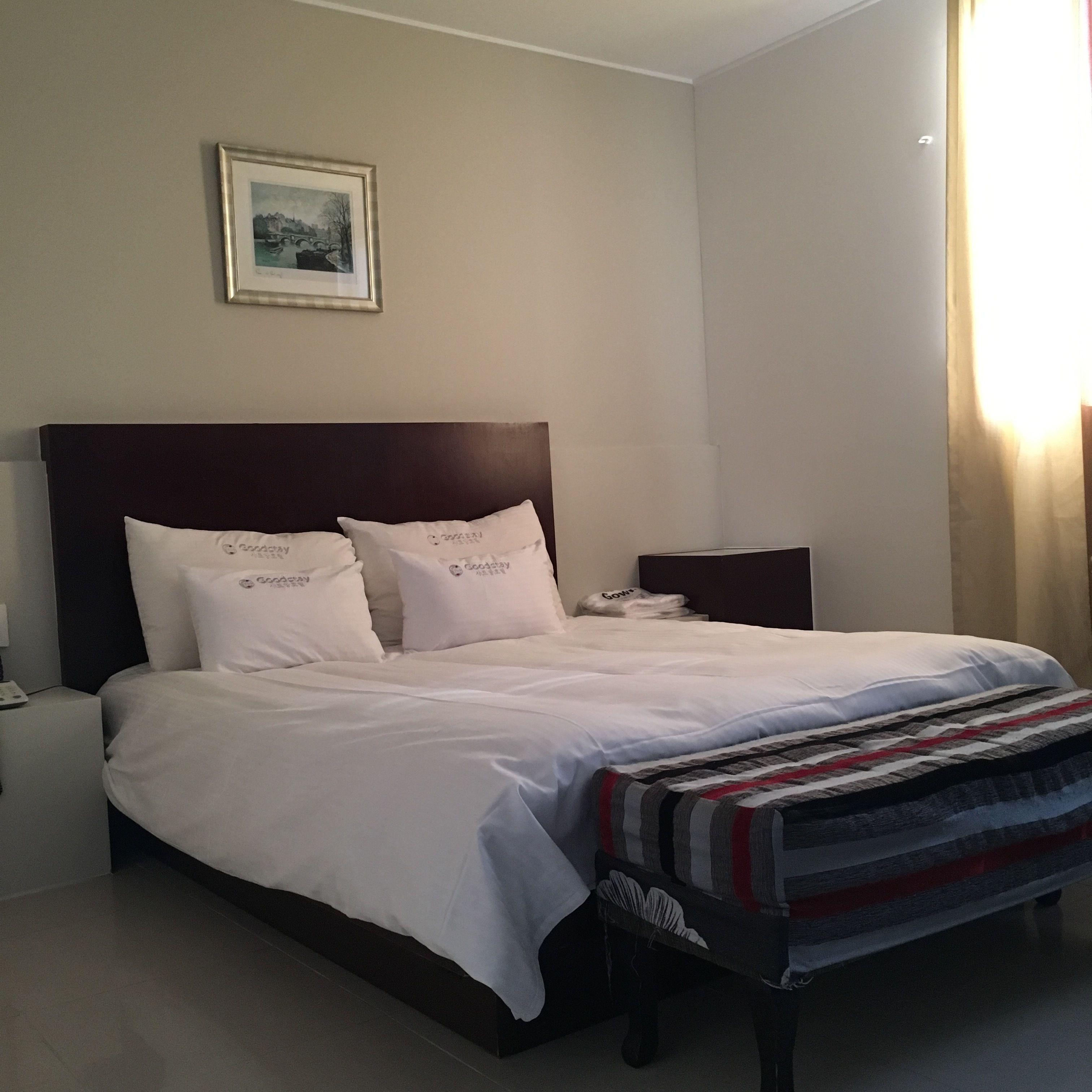 A neatly made bed with white bedding and pillows, a bedside table with a lamp, and a framed picture on the wall.