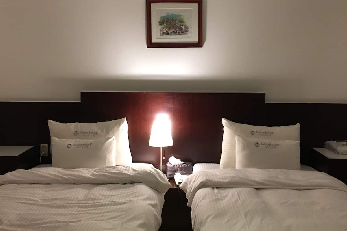 Une chambre d’hôtel avec deux lits, une table de chevet, une lampe et un tableau encadré au mur.