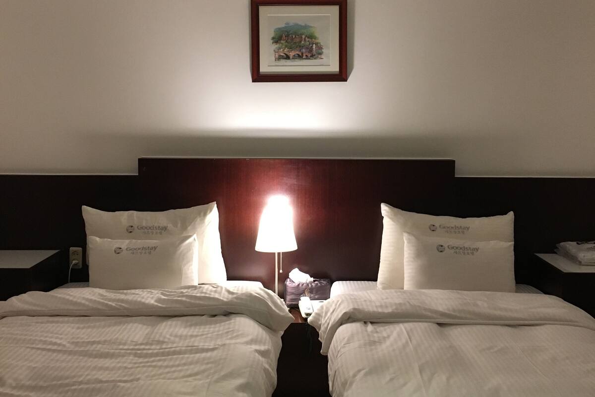Une chambre d’hôtel avec deux lits, une table de chevet avec une lampe et un tableau encadré au mur.