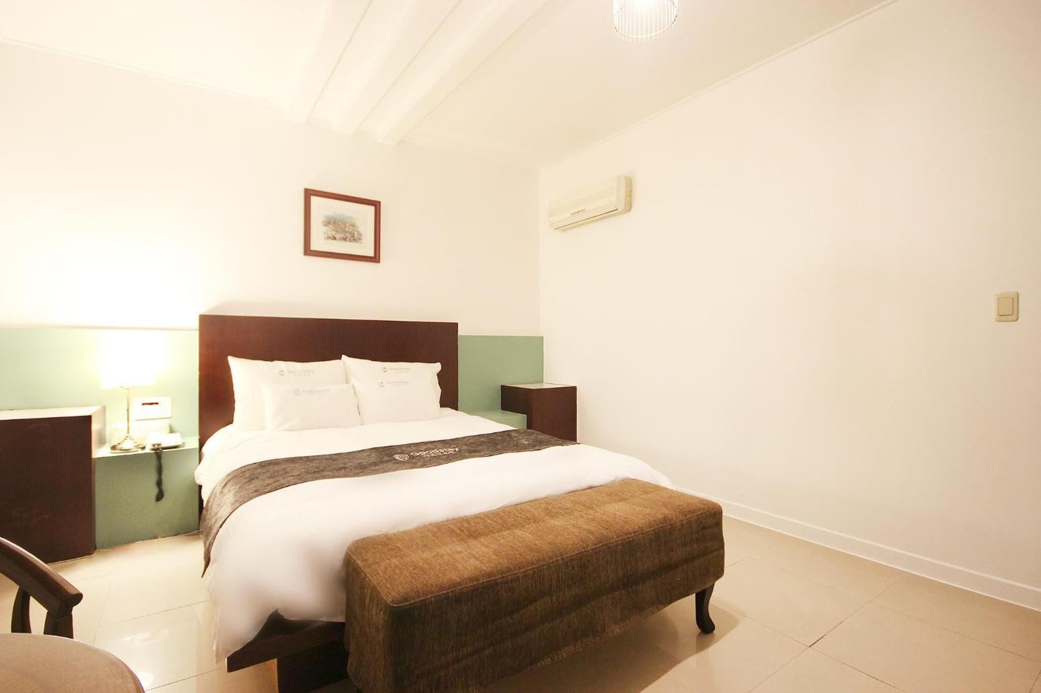 A hotel room with a bed, bedside tables, a bench, a wall-mounted picture, and a ceiling light.