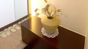A hallway with a framed picture on the wall, a vase with dried flowers on a console table, and a row of slippers on the floor. - Charmant Hotel (Mokpo)