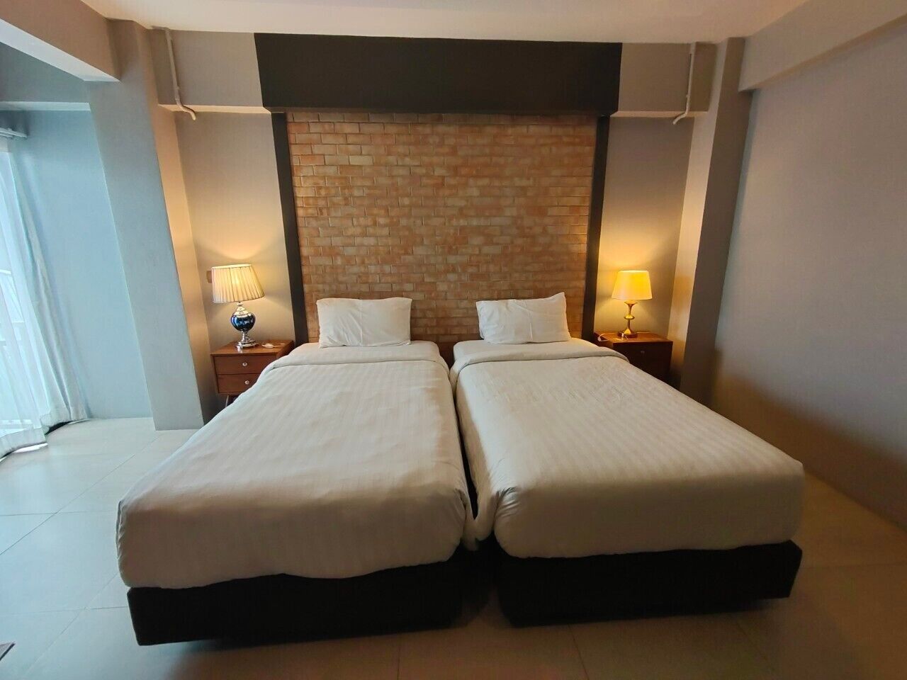 Habitación doble con dos camas, una pared decorativa de ladrillo y lámparas de noche.