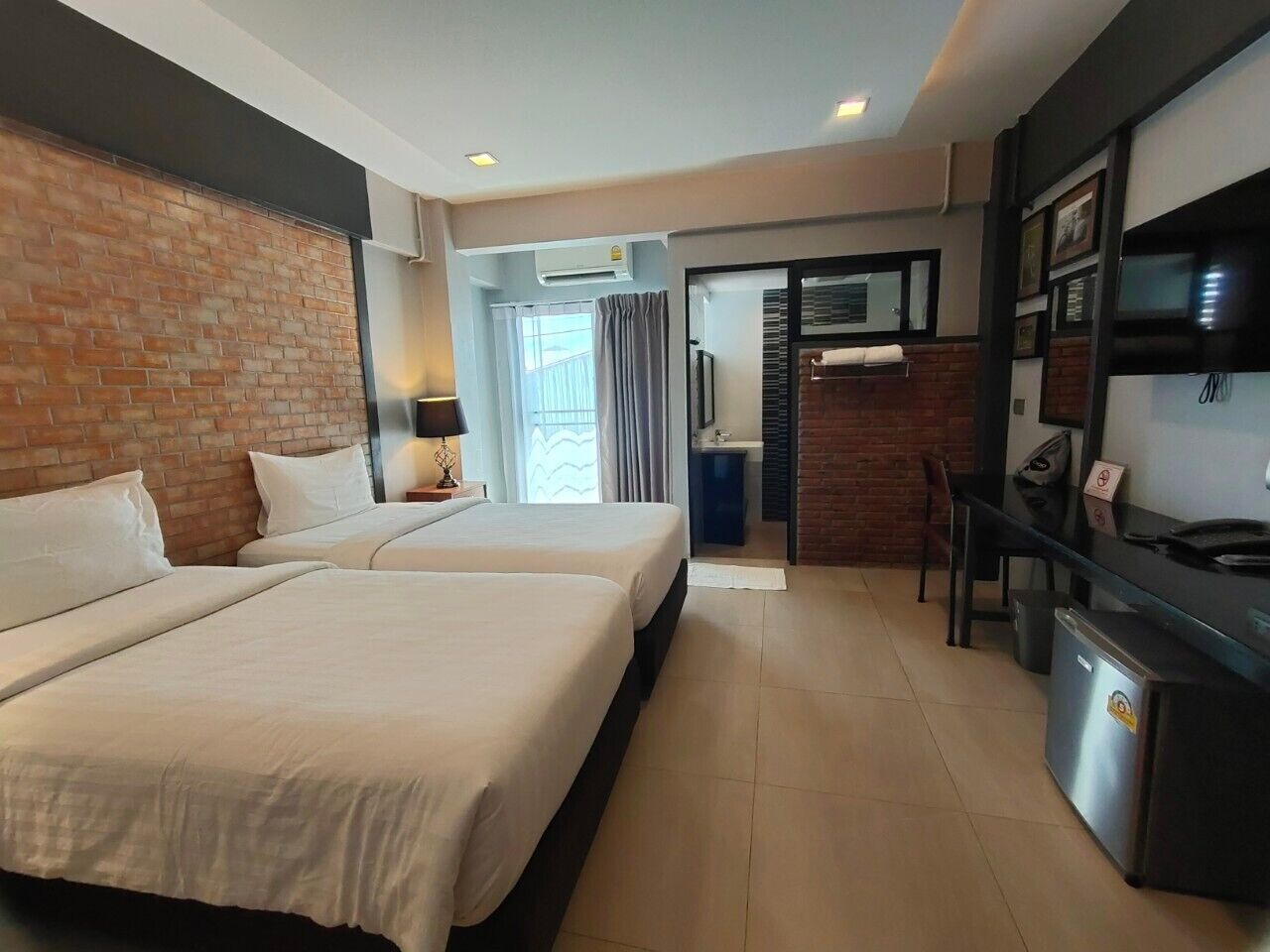 A hotel room with two beds, a desk, a small kitchenette, and a bathroom visible through an open door.