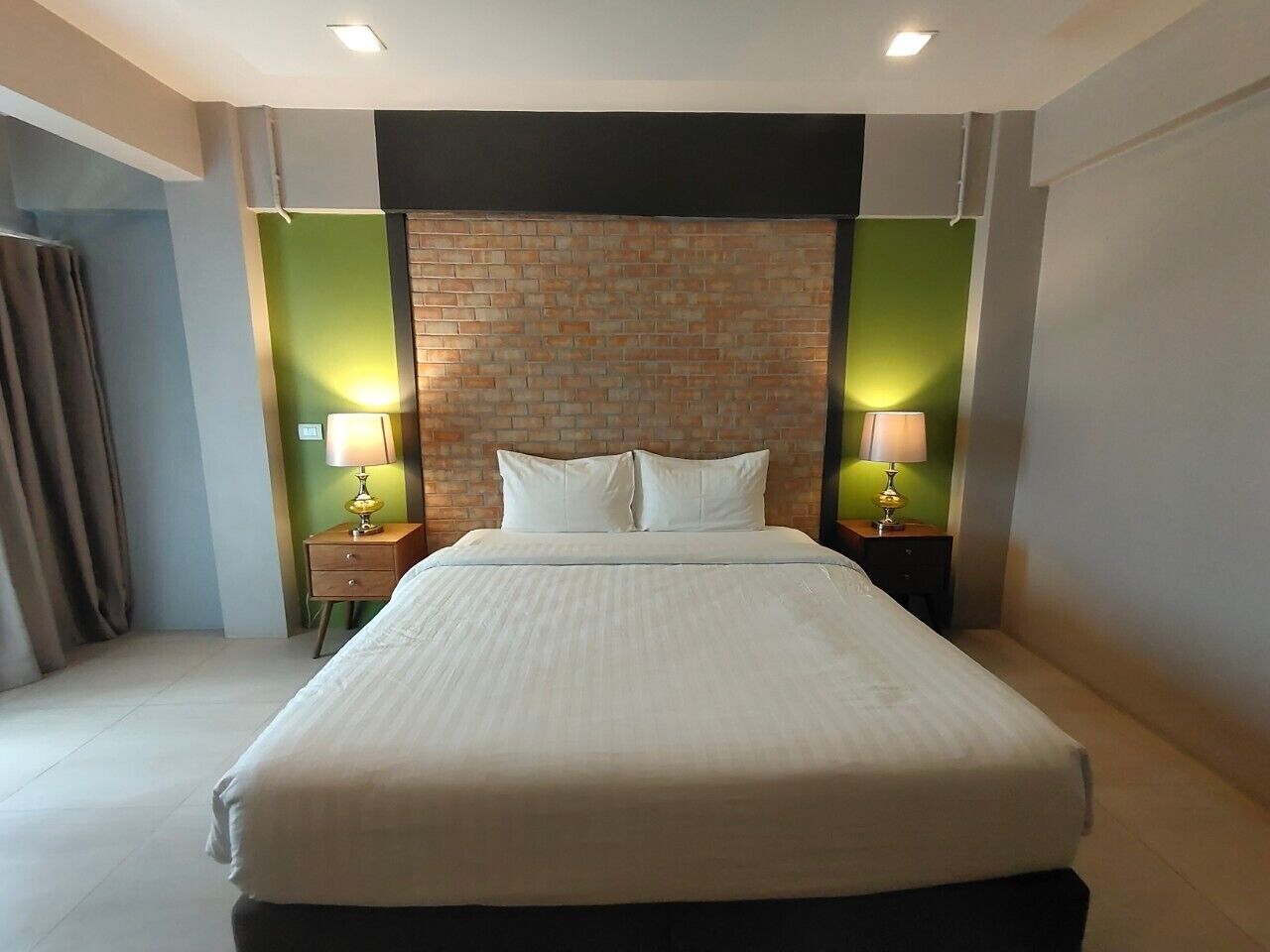 Une chambre d’hôtel avec un grand lit, deux tables de chevet avec des lampes, un mur d’accent en briques et des panneaux muraux verts.
