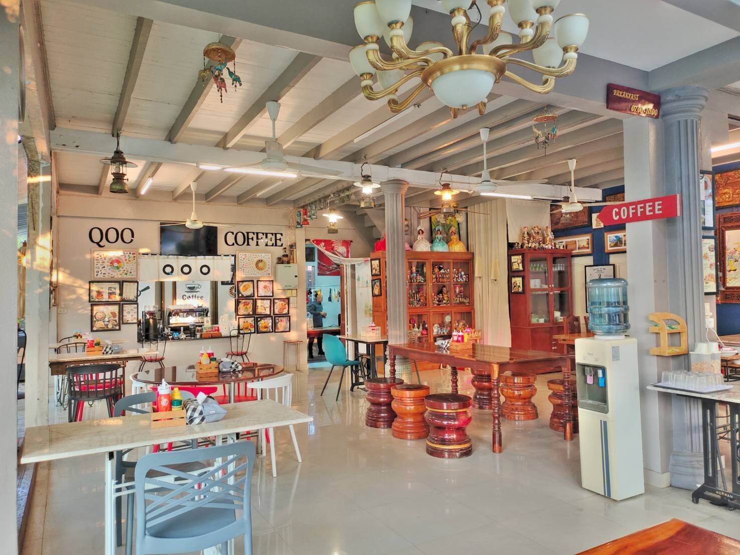 Interior de una cafetería con mesas, sillas, mostrador de café y un letrero que indica la zona de café.