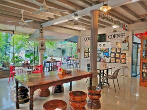 A modern coffee shop with a central wooden table, red chairs, and a sign indicating no pressure over cappuccino.