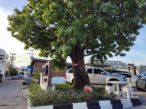 A tree-lined street with parked cars and a building with a sign. - Qoo Hotel (Buriram)