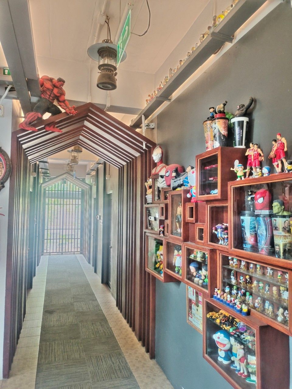 A corridor with a patterned floor leading to a gate, shelves with figurines, and a hanging light fixture.