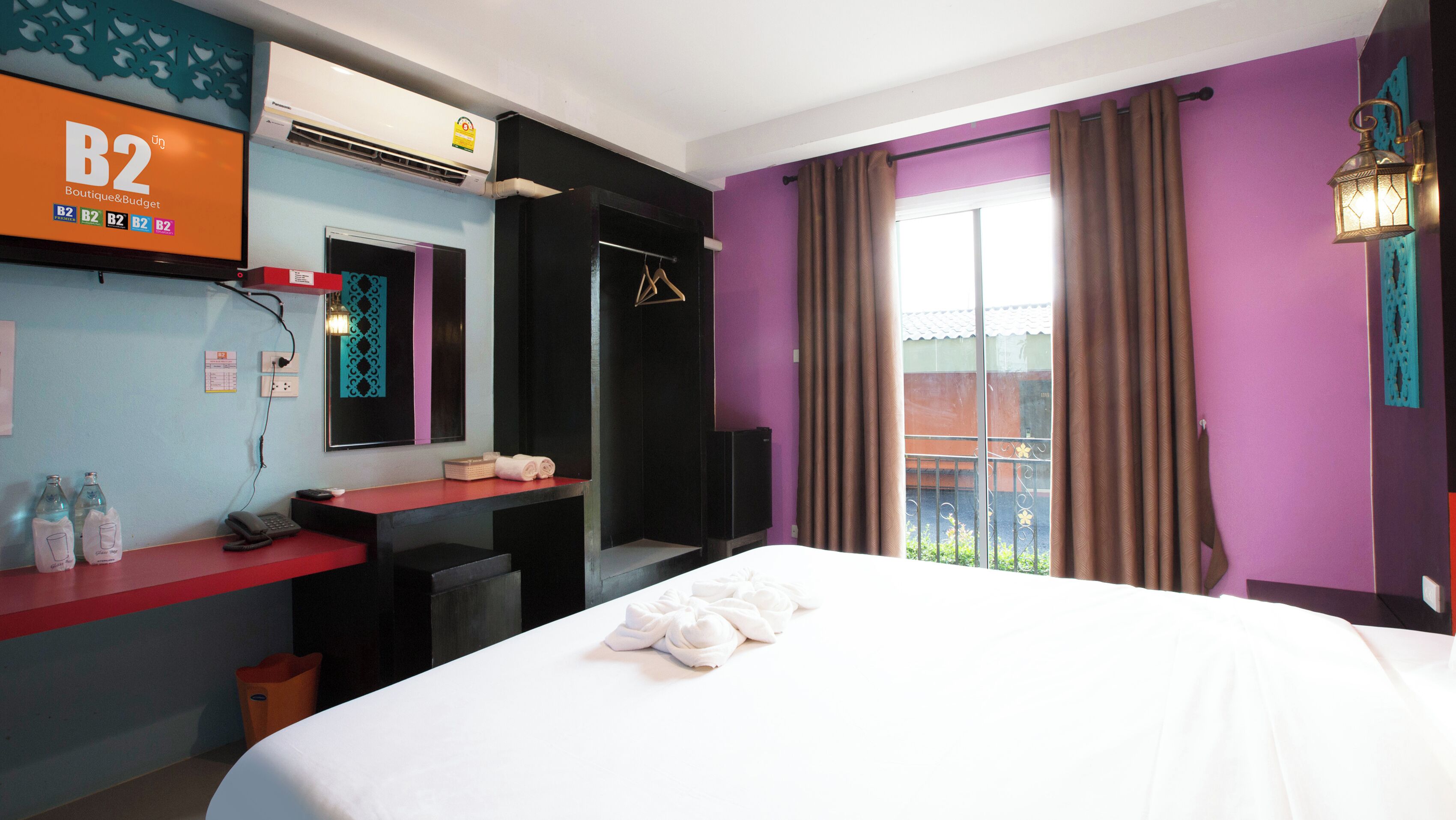 Habitación de hotel con cama, escritorio con teléfono, espejo y ventana con cortinas.
