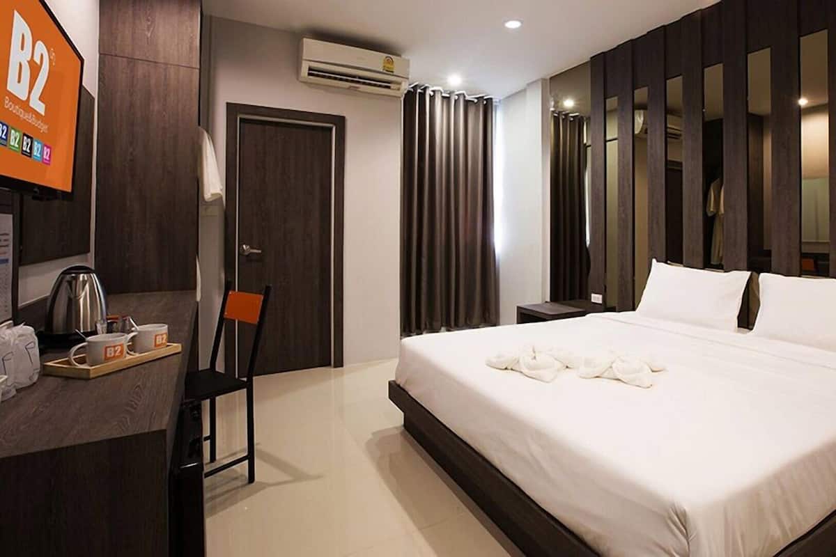 A hotel room with a bed, a desk with a coffee maker, a chair, a wardrobe, and a mirror.