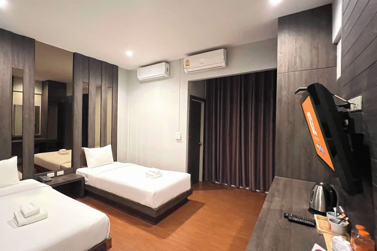 A hotel room with two beds, a desk with a kettle, a TV, and an air conditioning unit.