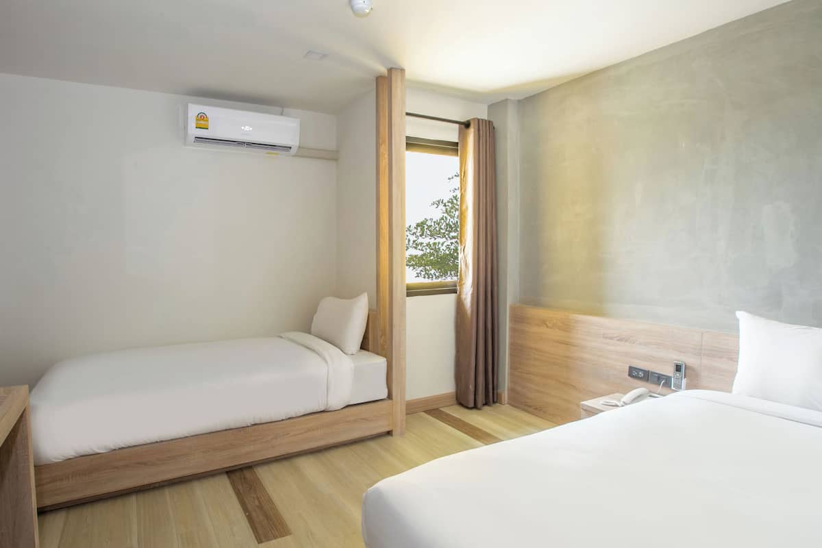 A hotel room with two beds, a wooden headboard, a window with curtains, and an air conditioning unit.