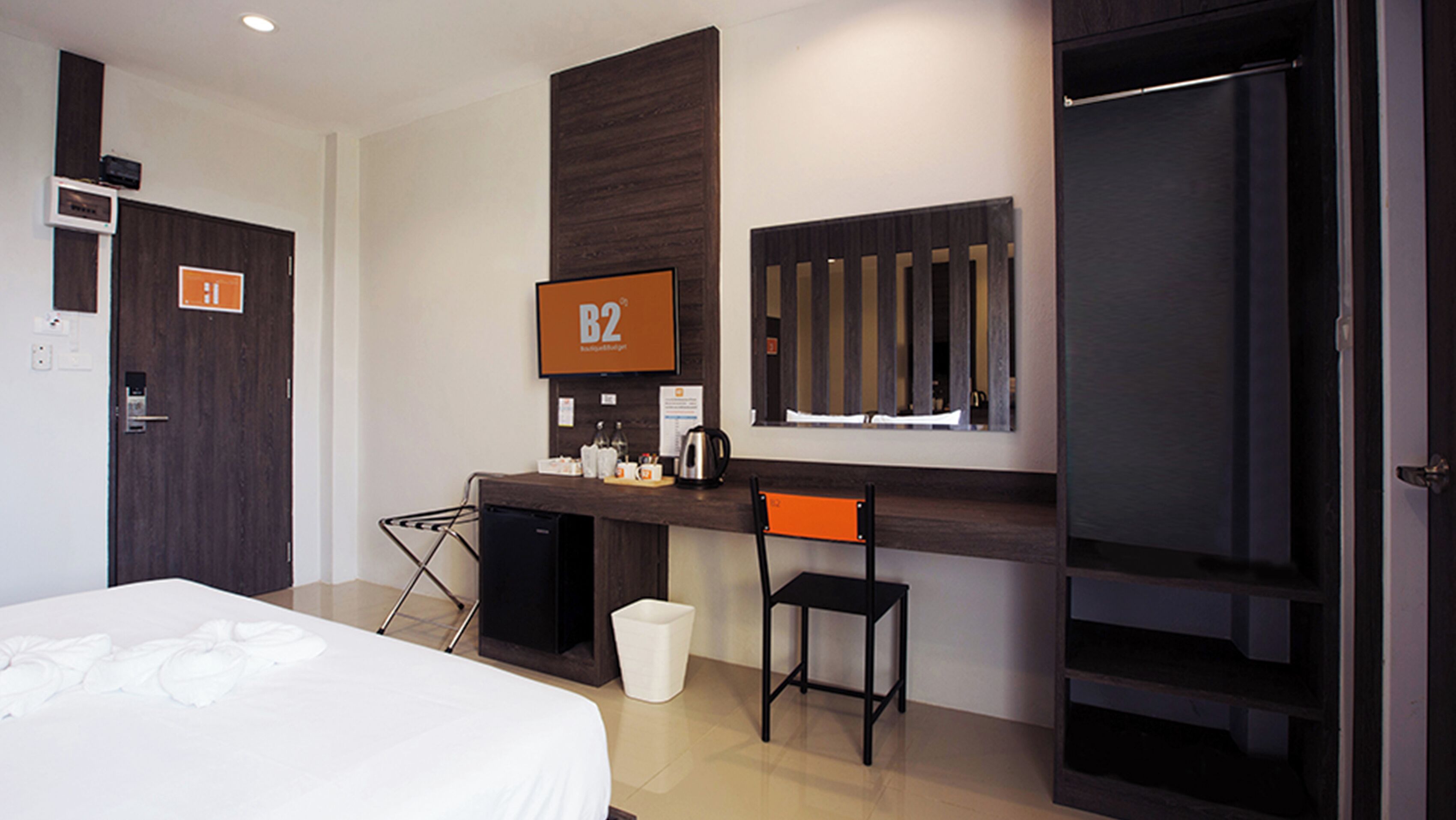 Habitación de hotel con cama, escritorio con cafetera, silla, un pequeño cubo de basura y armario.