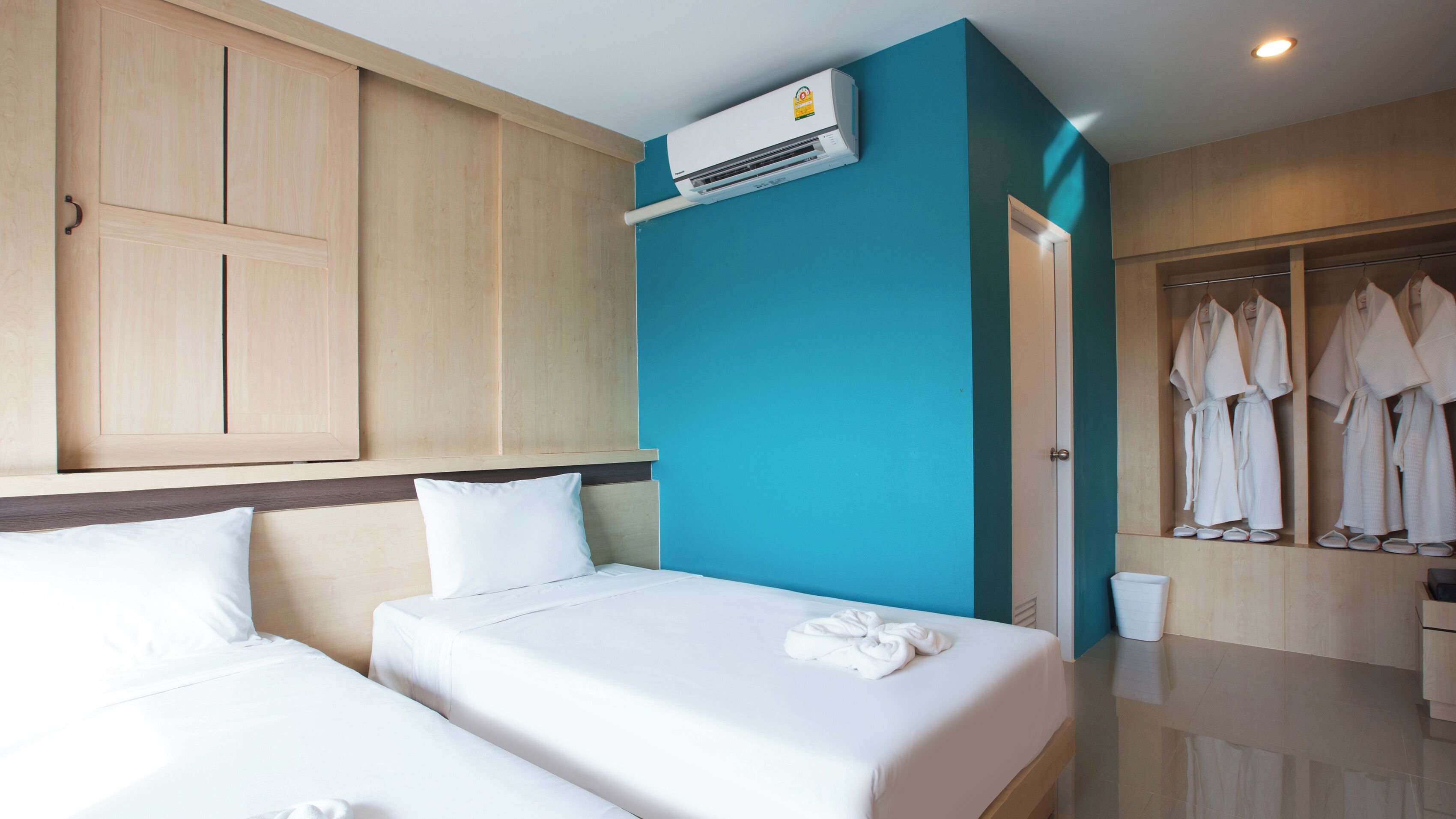 A hotel room with two beds, a wardrobe, an air conditioning unit, and a robe and slippers rack.