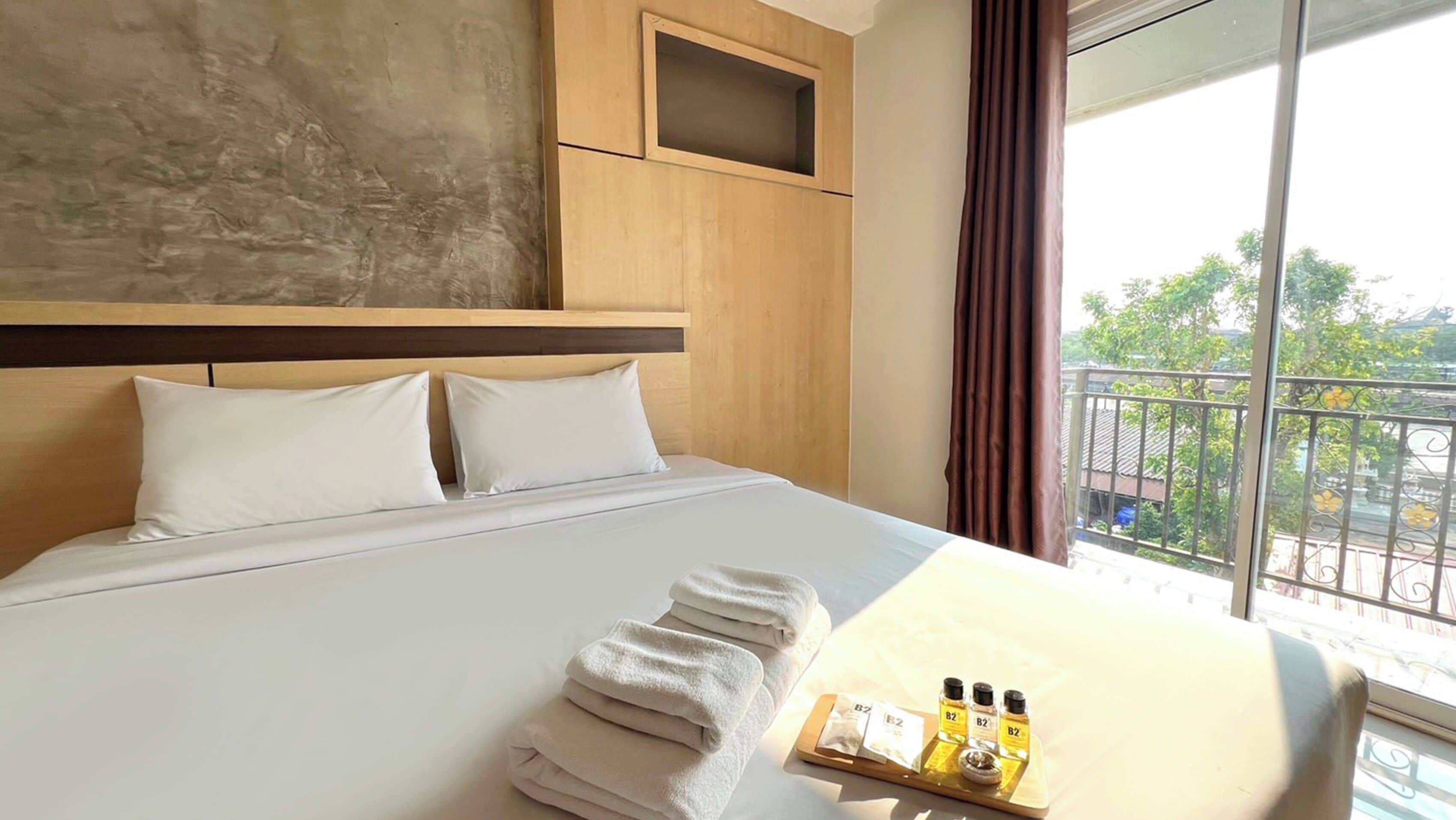 Ein Hotelzimmer mit einem großen Bett, einem Holzkopfteil, Blick ins Freie und einem Tablett mit Toilettenartikeln.