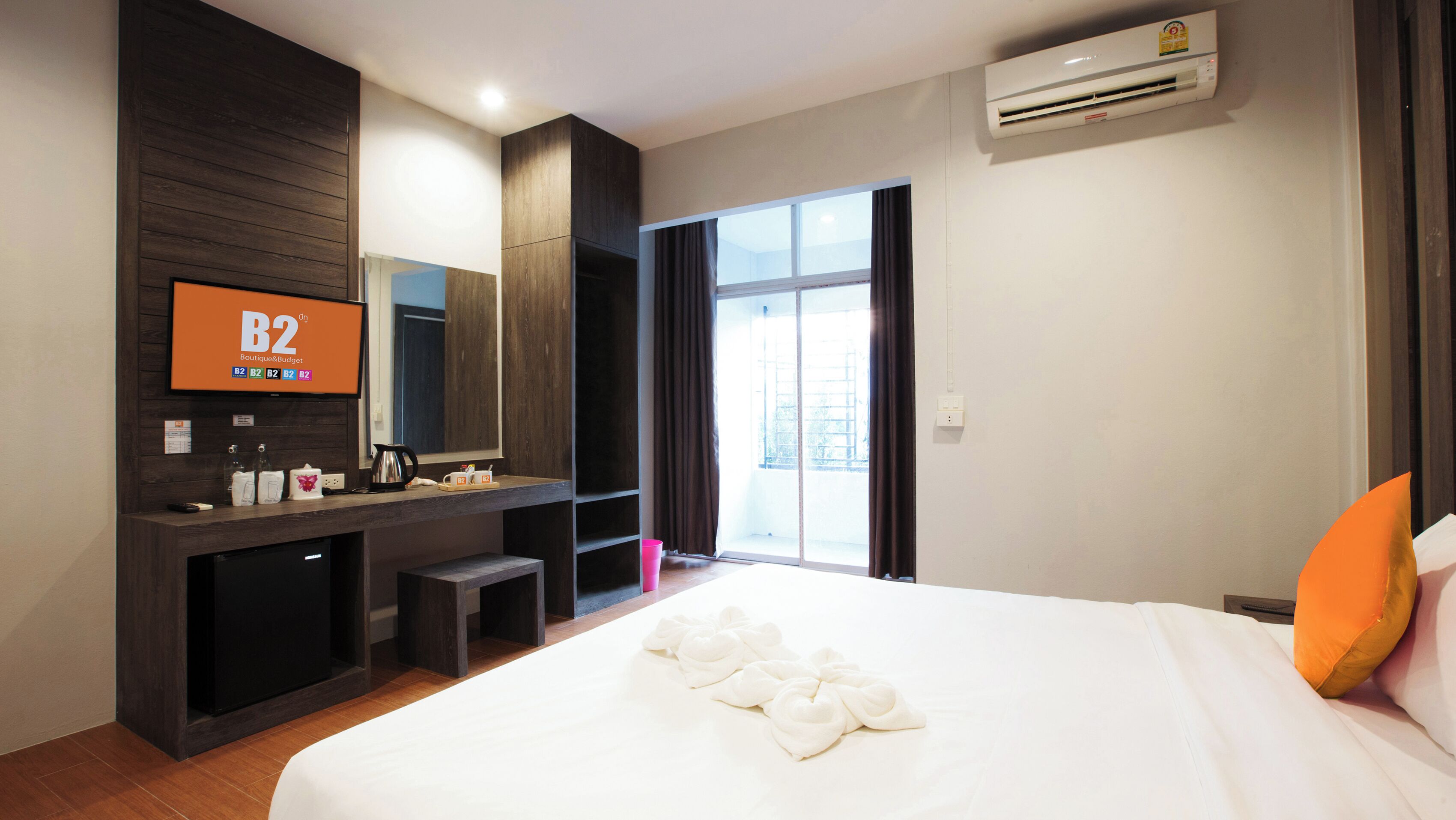 A hotel room with a large bed, a TV on the wall, a desk with a mirror, and a window with curtains.