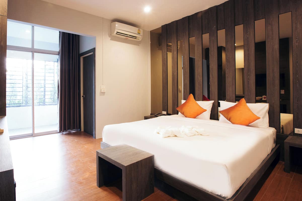 A hotel room with a large bed, a small bedside table, a bedside lamp, a window with curtains, a sliding door, and a wooden wall paneling.