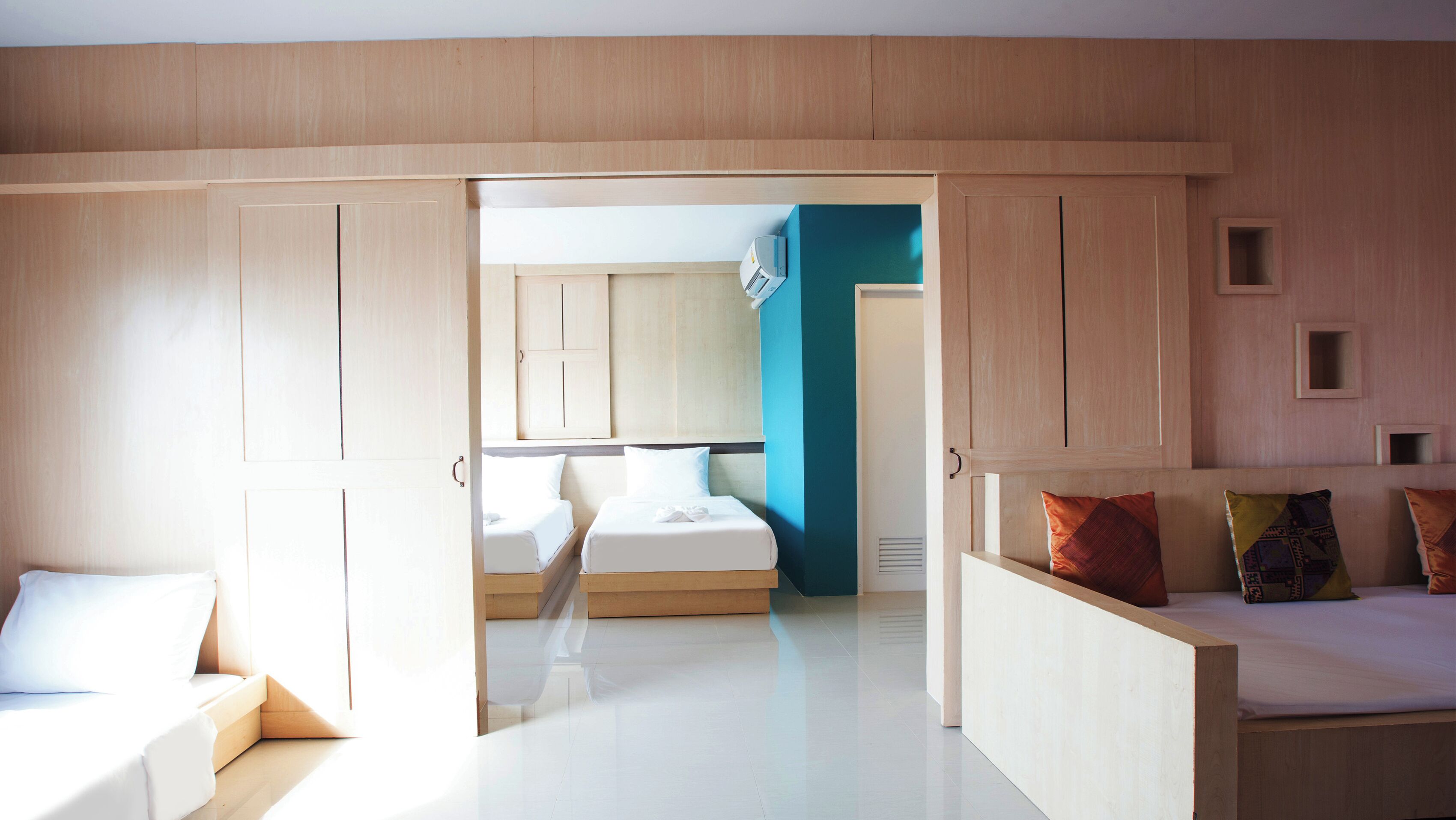 Ett modernt hotellrum med en garderob i trä, en säng med vita sängkläder, en liten sittgrupp och utsikt in i ett annat rum med en blå accentvägg.
