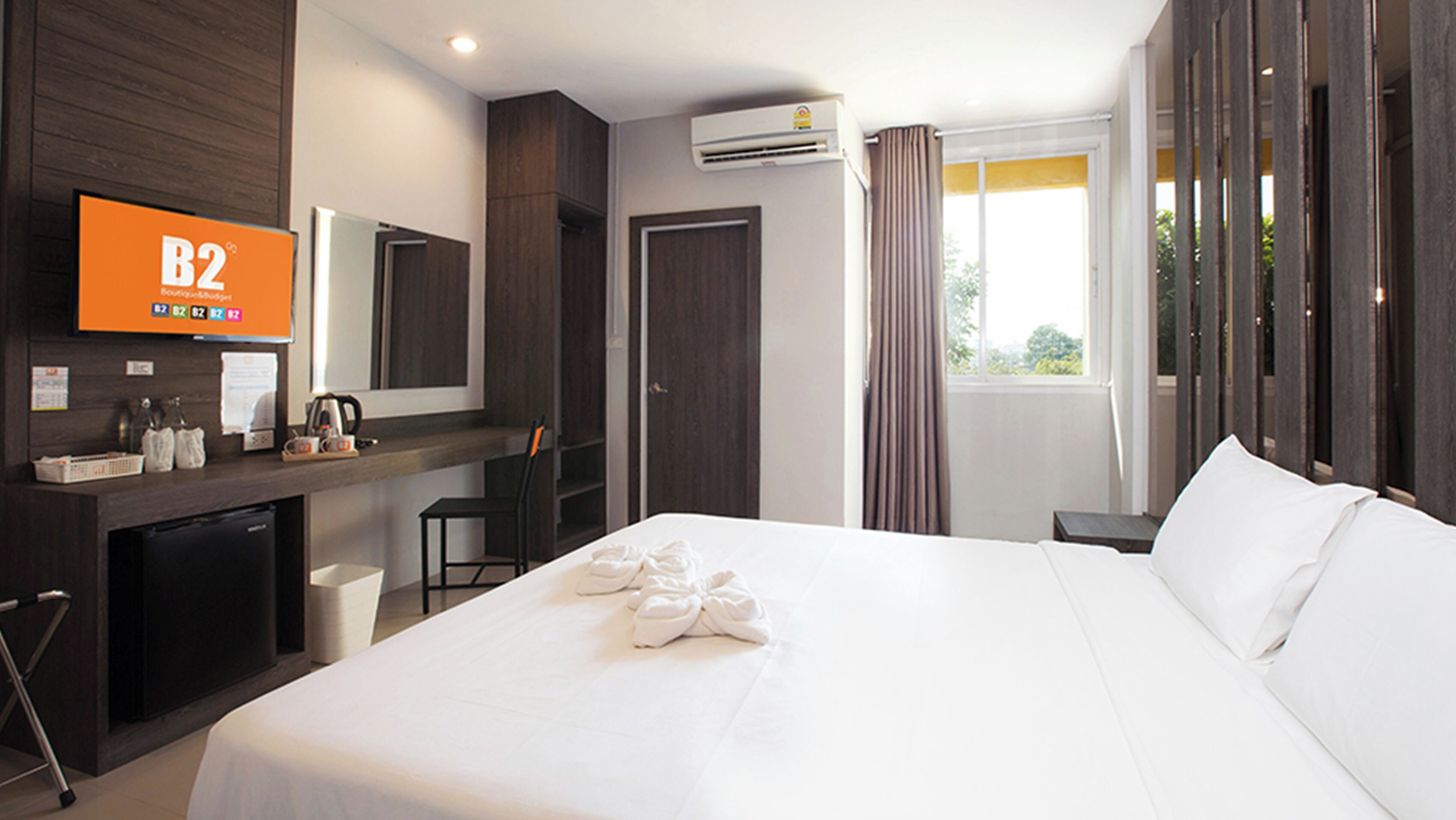 A hotel room with a large bed, a desk with a chair, a television, and an air conditioning unit.