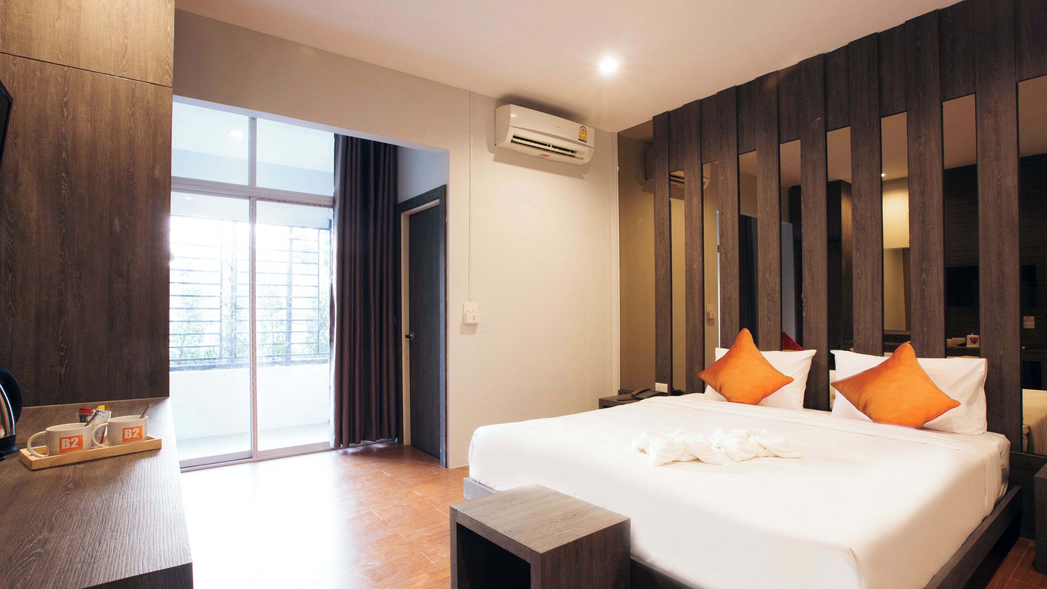 Habitación de hotel con una cama grande, dos almohadas, una mesita de noche, un escritorio con silla, una ventana con cortinas y un equipo de aire acondicionado.