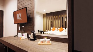 A hotel room with a wooden counter, a television displaying 'B2 Boutique & Budget', and a bed with orange pillows. - B2 Buriram Boutique & Budget Hotel (Buriram)
