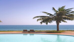 Piscina con dos sillas de descanso y una palmera, con vista al océano.