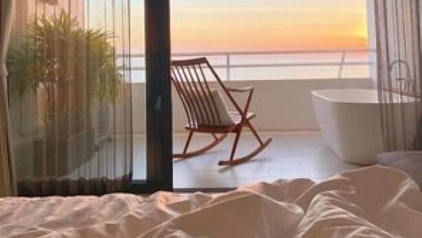 Un dormitorio con vista al atardecer sobre el océano, una mecedora y una bañera.
