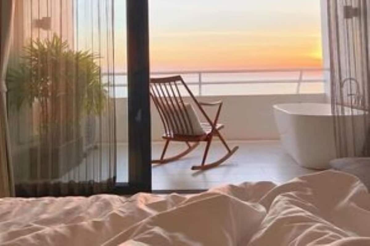 Ein Schlafzimmer mit Blick auf den Sonnenuntergang über dem Meer, ein Schaukelstuhl und eine Badewanne.