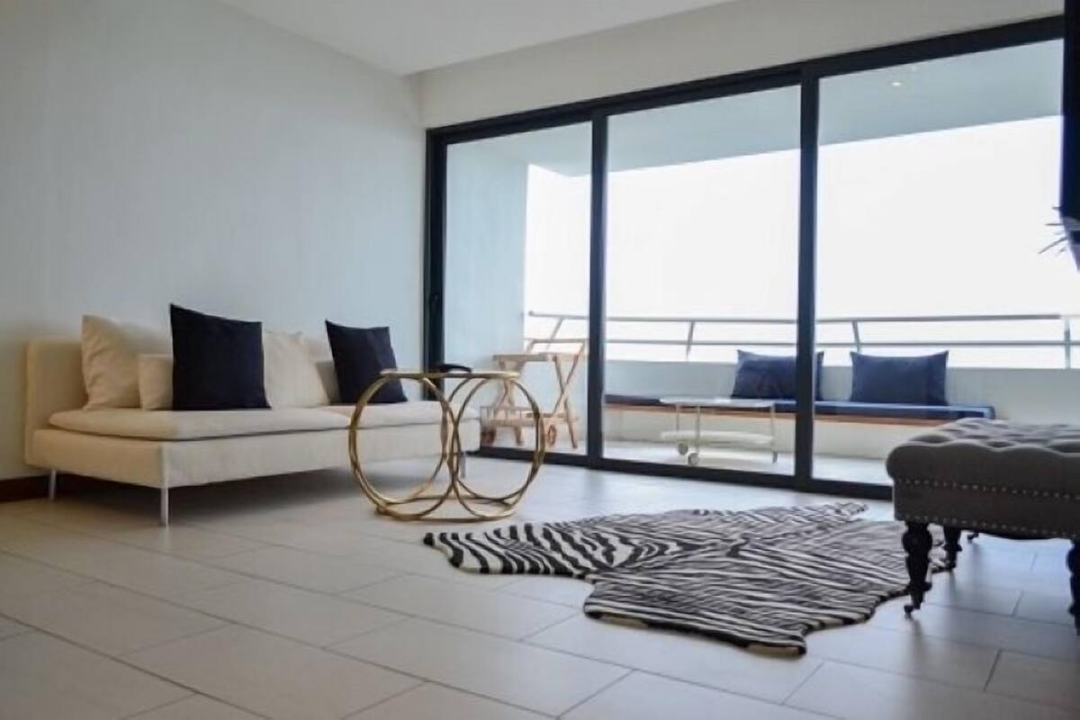 Ein modernes Wohnzimmer mit einer Couch, einem Zebra-Teppich und einer großen Glasdoor, die auf einen Balkon führt.