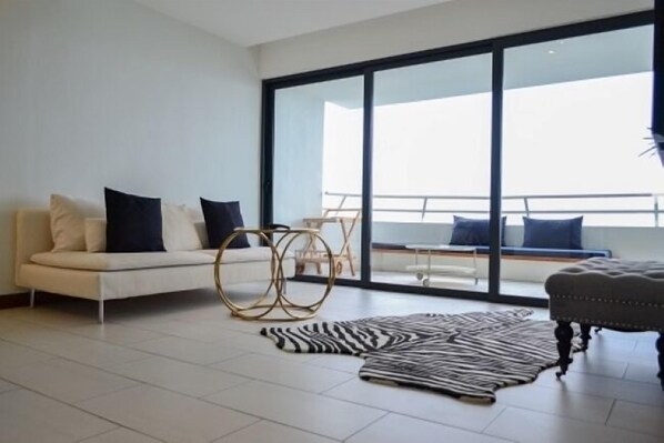 Un salón moderno con un sofá, un alfombra de cebra y un amplio ventanal que da a un balcón.