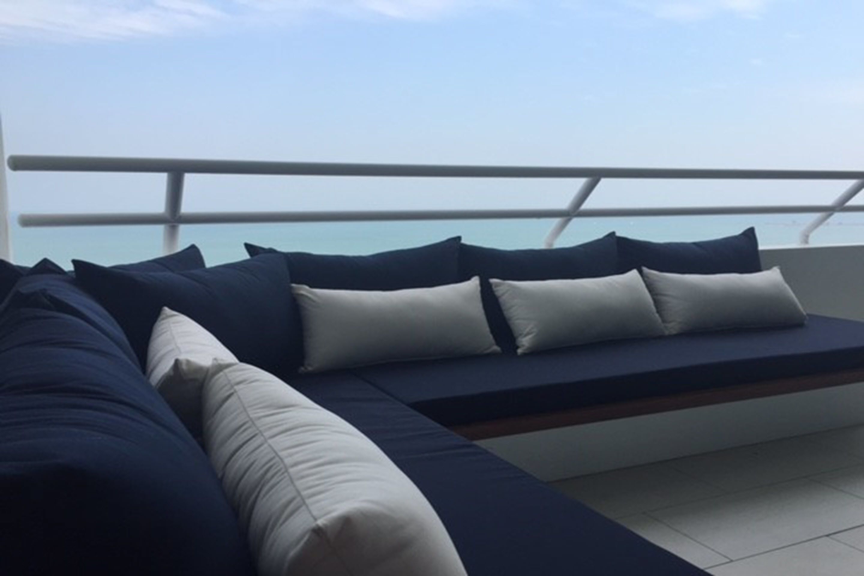 A modern outdoor seating area with a view of the sea, featuring a sofa with cushions and a railing.