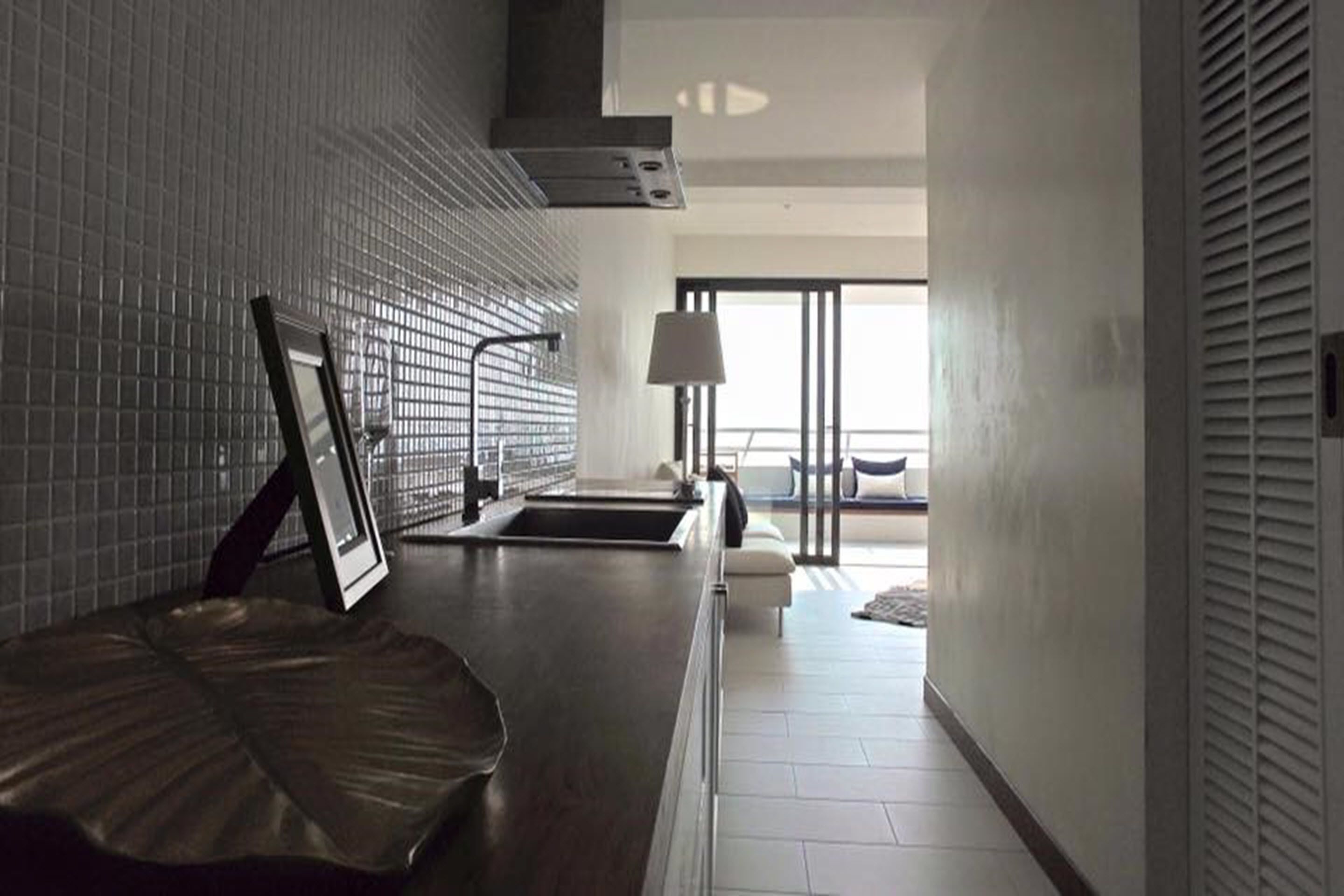 A modern kitchen with a tiled backsplash, a dark countertop, and a view of a balcony through a large window.