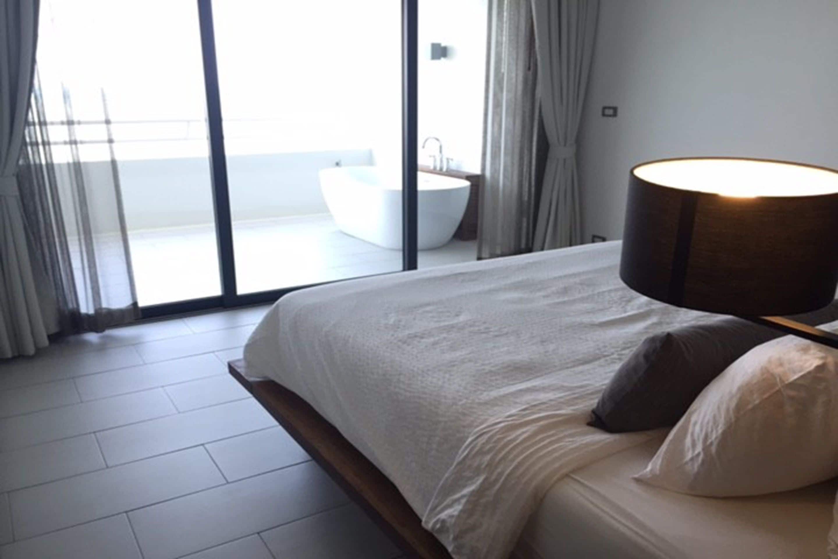 Un dormitorio moderno con una cama grande, una lámpara de noche y vista a un baño a través de una puerta de cristal.